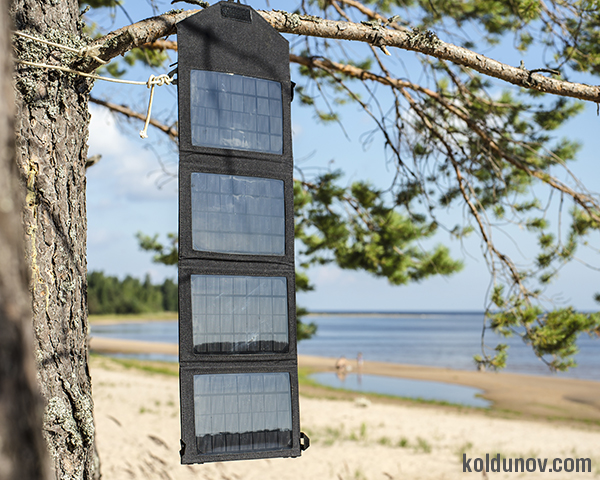 Portable foldable solar panel battery hanging on the outdoors on a pine tree on the seashore near the sandy beach